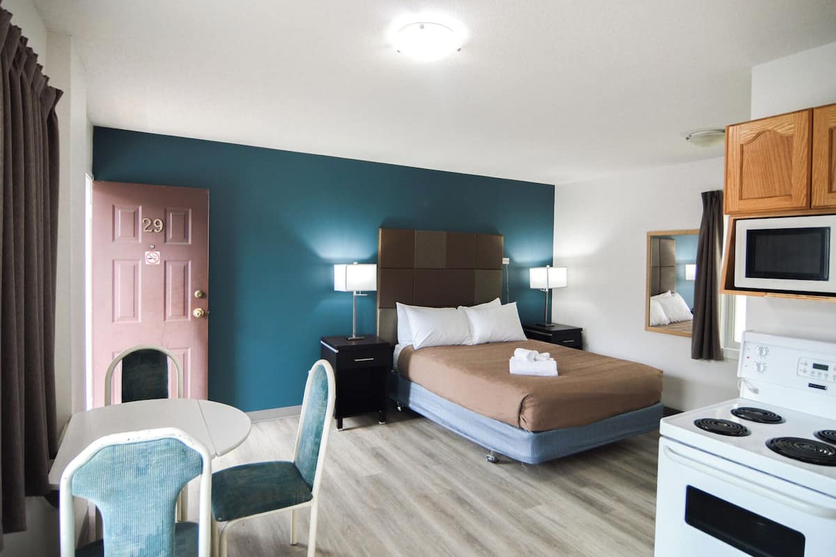 A hotel room with a bed, bedside lamps, a microwave, a small table with a chair, and a door with a number.