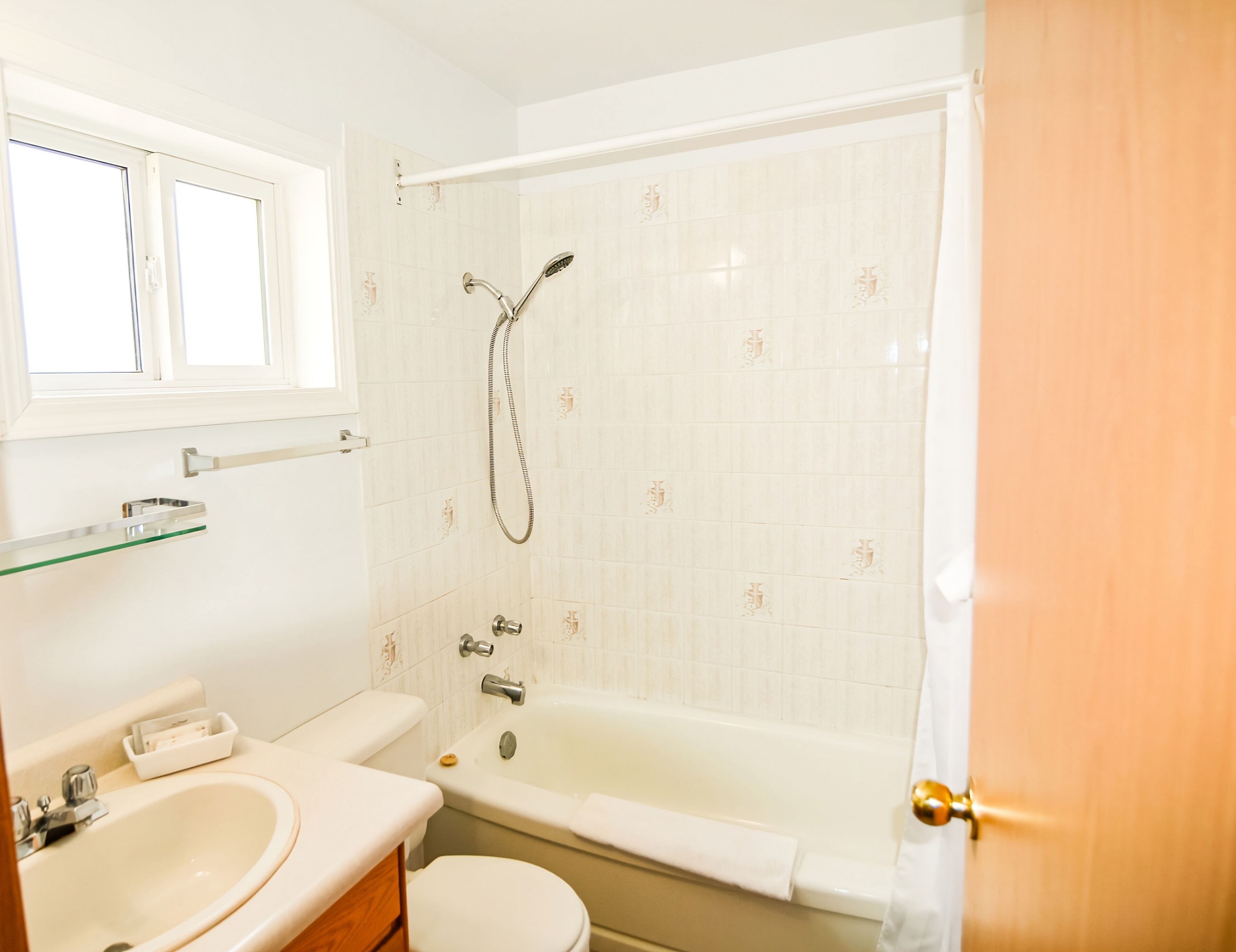 Un bagno con vasca, water, lavandino e una finestra sopra il lavandino.