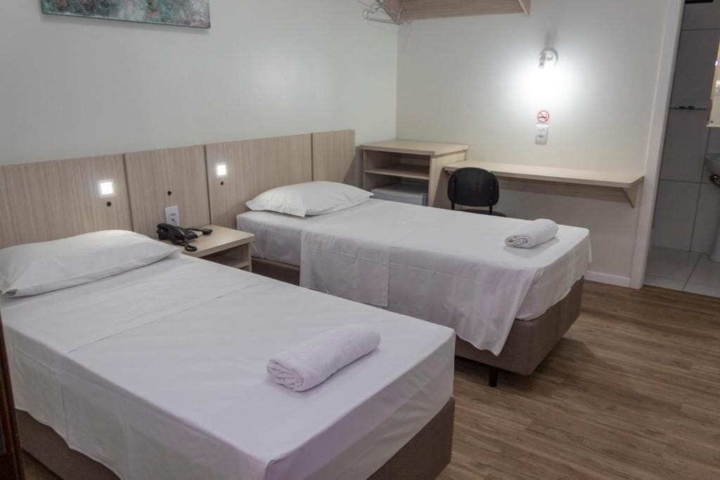 A hotel room with two single beds, a desk, a chair, and a small workspace.