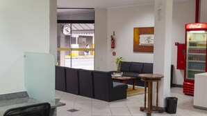 A lobby with a reception desk, a sofa, a small table, a plant, a Coca-Cola refrigerator, and a fire extinguisher. - Hotel Vitória (Itajai)
