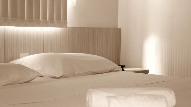 A neatly made bed with white linens, a bedside table, and a headboard. - Hotel Vitória (Itajai)