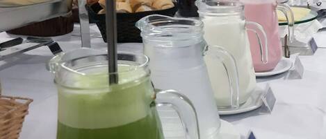 Una mesa de buffet con diversos alimentos y bebidas, incluyendo una bebida verde, una bebida blanca y una bebida rosa.