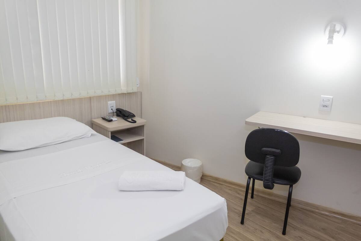 Una habitación de hotel con cama, escritorio, silla, teléfono y lámpara de pared.