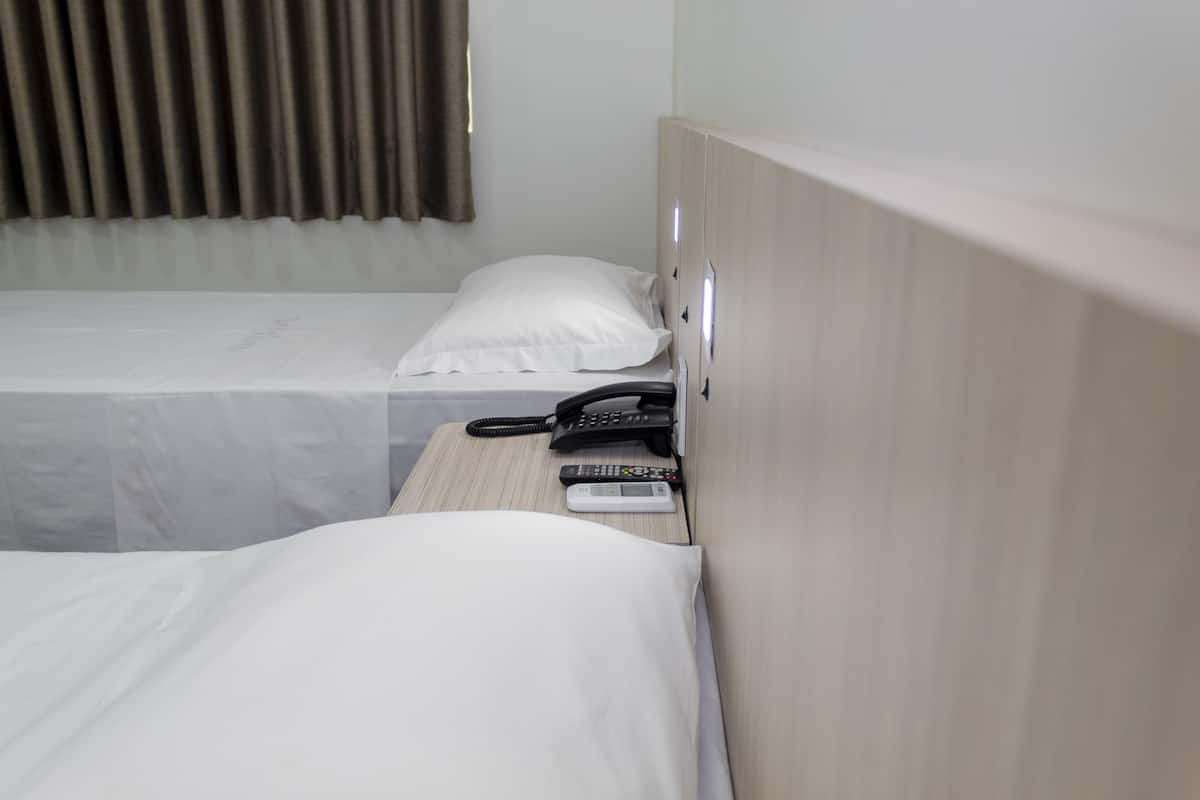 Habitación de hotel con dos camas, cada una con ropa blanca, teléfono junto a la cama y un control remoto en la mesita de noche.