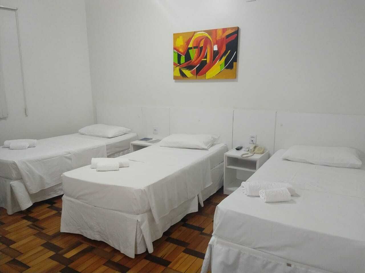 A hotel room with three single beds, a wooden floor, and a colorful abstract painting on the wall.