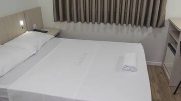 A hotel room with a neatly made bed, a bedside table with a lamp, and a curtain.