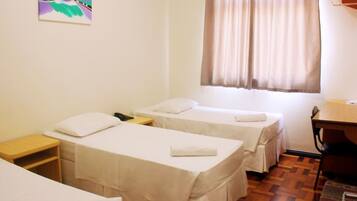 A hotel room with two single beds, a wooden desk, a chair, and a window with curtains.
