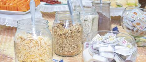 Una mesa de buffet con diversas opciones de comida, incluyendo tarros de granola, un tazón de malvaviscos y un plato de fruta cortada.