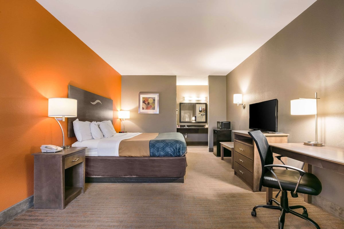 A hotel room with a bed, desk, chair, and a TV.