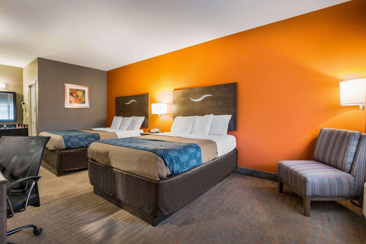 A hotel room with two beds, a desk, and a chair.