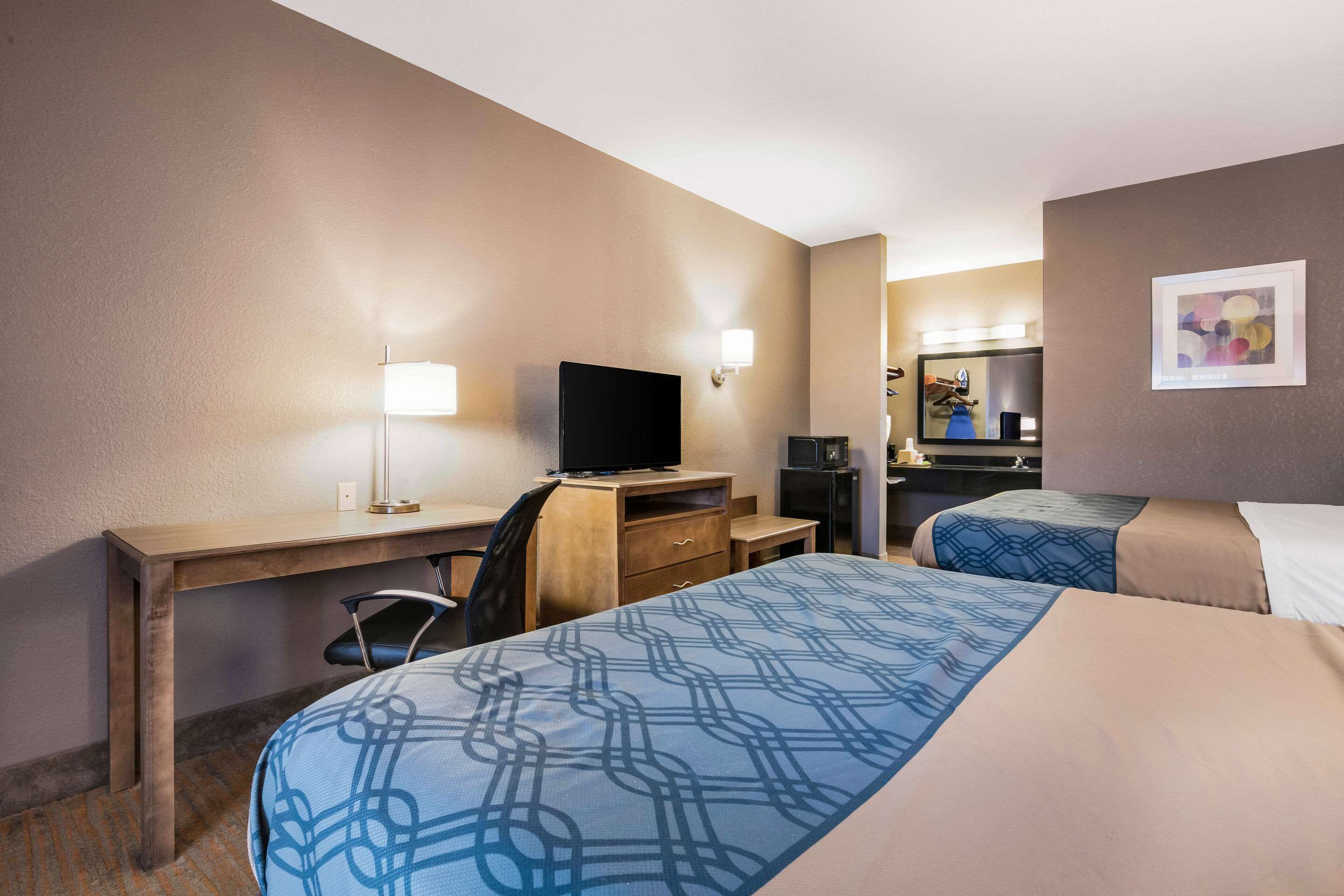 A hotel room with two beds, a desk, a television, and a mirror.