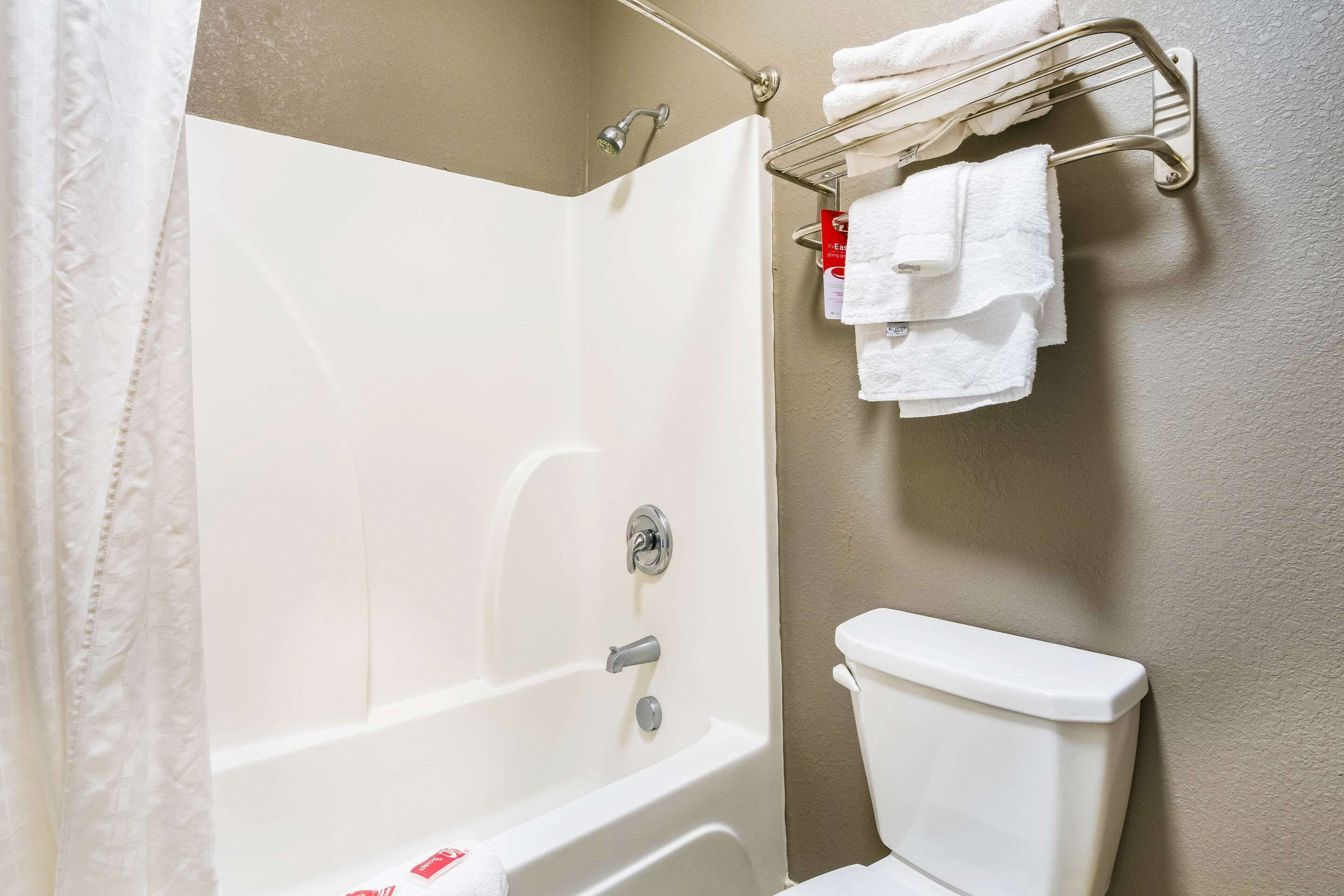 A bathroom with a white bathtub, a toilet, and a towel rack with multiple white towels.