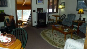 Uma sala de estar aconchegante com lareira, uma poltrona verde, um sofá xadrez e uma mesa de centro de madeira.