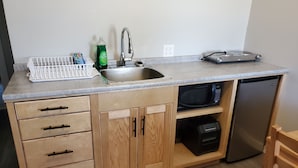 Una cocina compacta con un lavamanos, un microondas, un lavavajillas y armarios de madera.