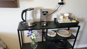 Una estantería metálica negra con una cafetera, un hervidor, un florero con flores y platos apilados.