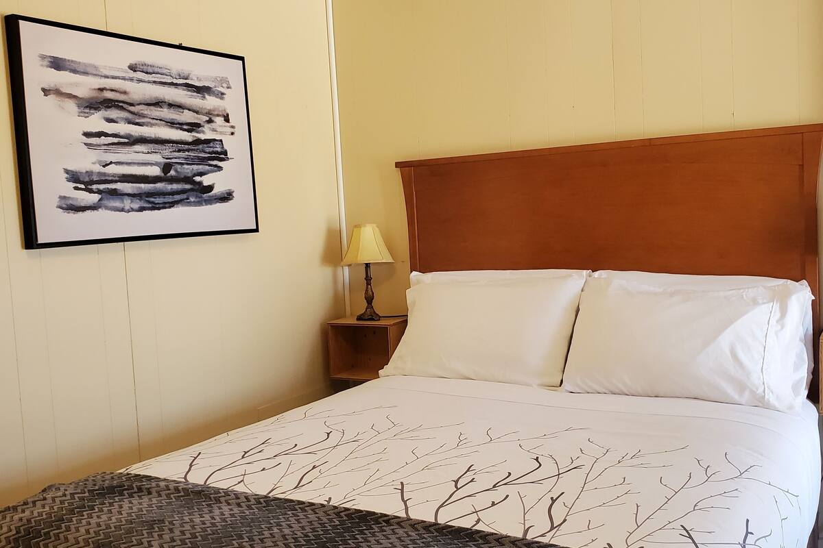 A hotel room with a bed, a nightstand, a lamp, and a framed abstract painting on the wall.