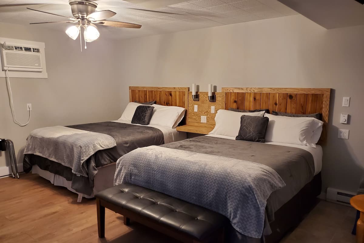 A bedroom with two beds, a bench, a ceiling fan, and an air conditioning unit.
