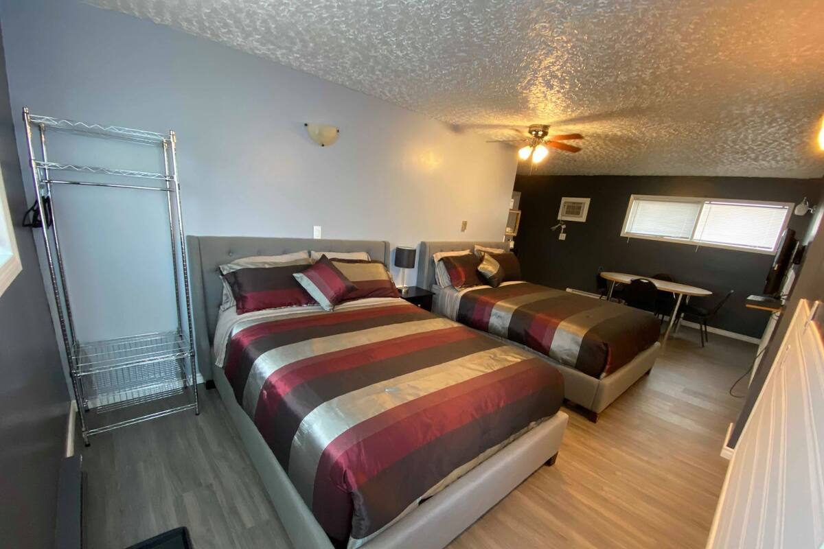 A hotel room with two beds, a desk, a chair, a ceiling fan, and a window.