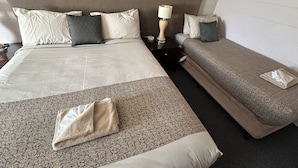 A hotel room with a large bed, a smaller bed, a nightstand with a lamp, and a folded towel on the floor. - Warren Motor Inn (Warren)
