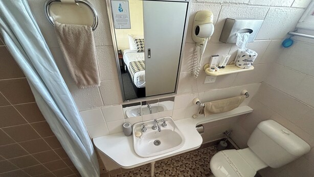 A bathroom with a sink, toilet, and hairdryer. - Warren Motor Inn (Warren)