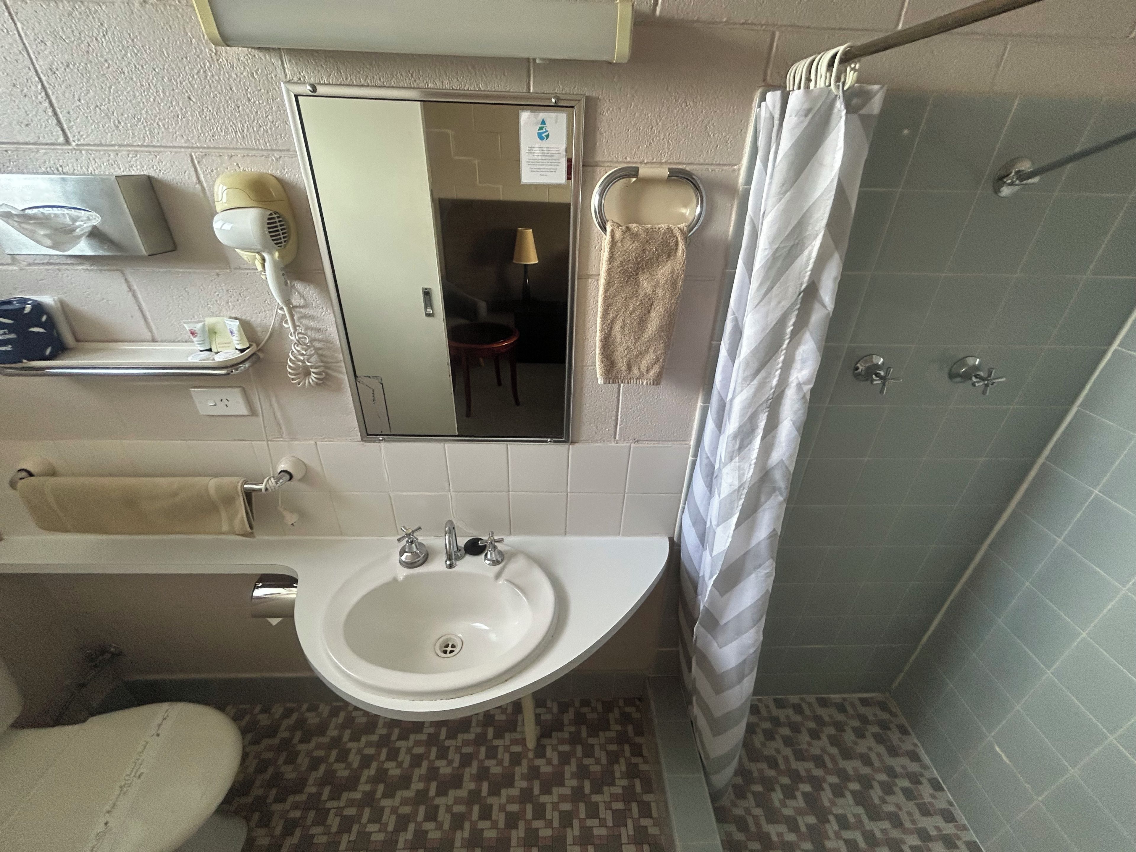 Een badkamer met een wastafel, spiegel, handdoekhouder en douchegordijn.