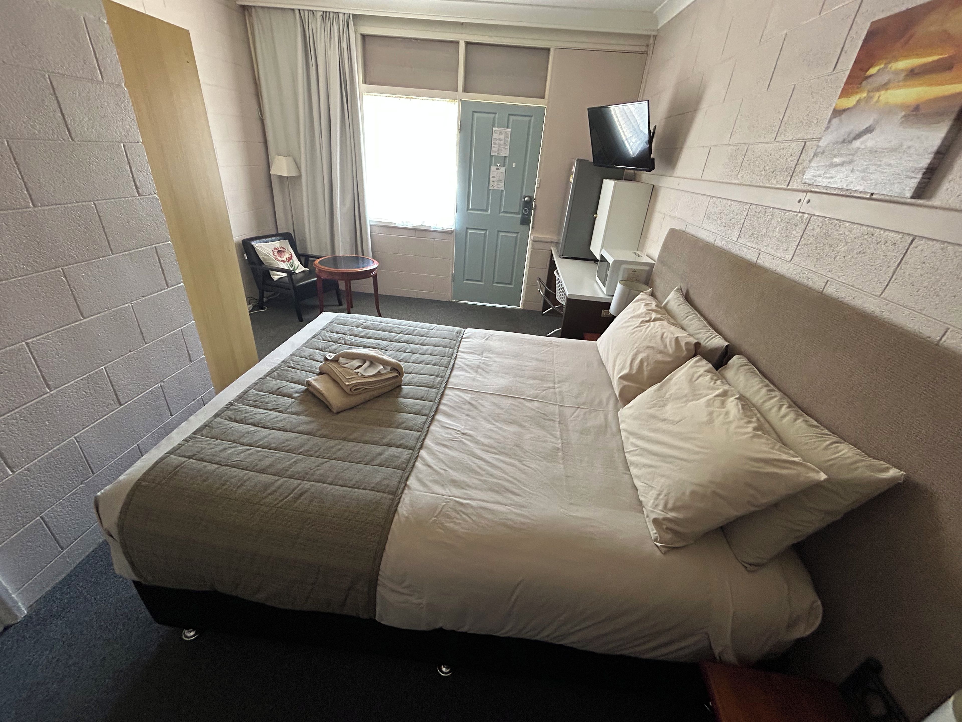 A hotel room with a bed, a television on a stand, a chair, and a desk with a computer.