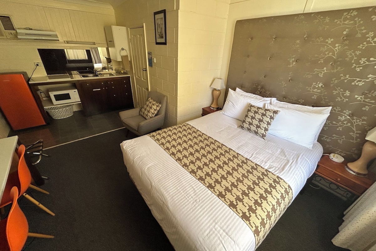 Une chambre d’hôtel avec un grand lit, un bureau équipé d’un micro-ondes, une chaise et une petite kitchenette.
