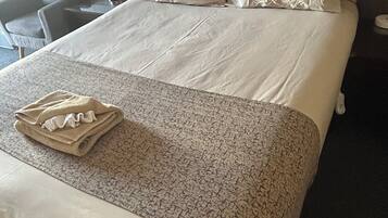 Una cama bien hecha con una colcha estampada, una toalla doblada y dos almohadas.