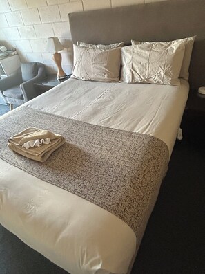 A neatly made bed with a patterned bedspread, a folded towel, and two pillows.