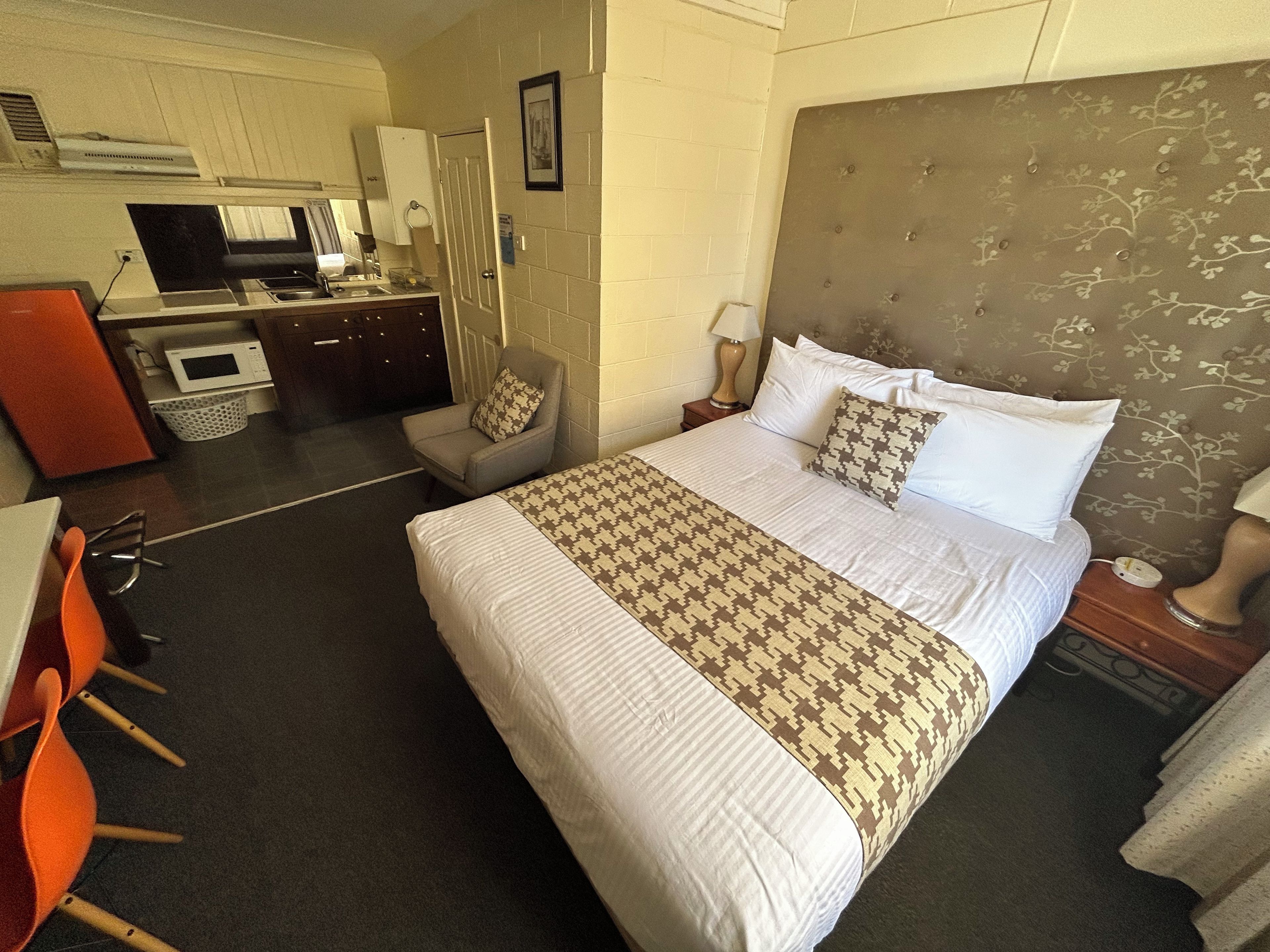 Een hotelkamer met een groot bed, een bureau met een magnetron, een stoel en een kleine kitchenette.