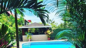 A swimming pool surrounded by lush tropical plants and a small gazebo. - Hotel Belvedere (Sámara)