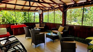 A covered outdoor seating area with wicker furniture, a fan, and a red table. - Hotel Belvedere (Sámara)