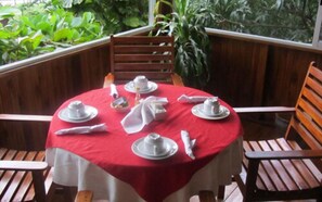A round table with a red tablecloth, white plates, and silverware, surrounded by wooden chairs. - Hotel Belvedere (Sámara)
