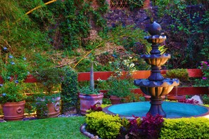 A garden with a fountain, potted plants, and a brick wall. - Chalet Boutique San Marcos (Cuernavaca)
