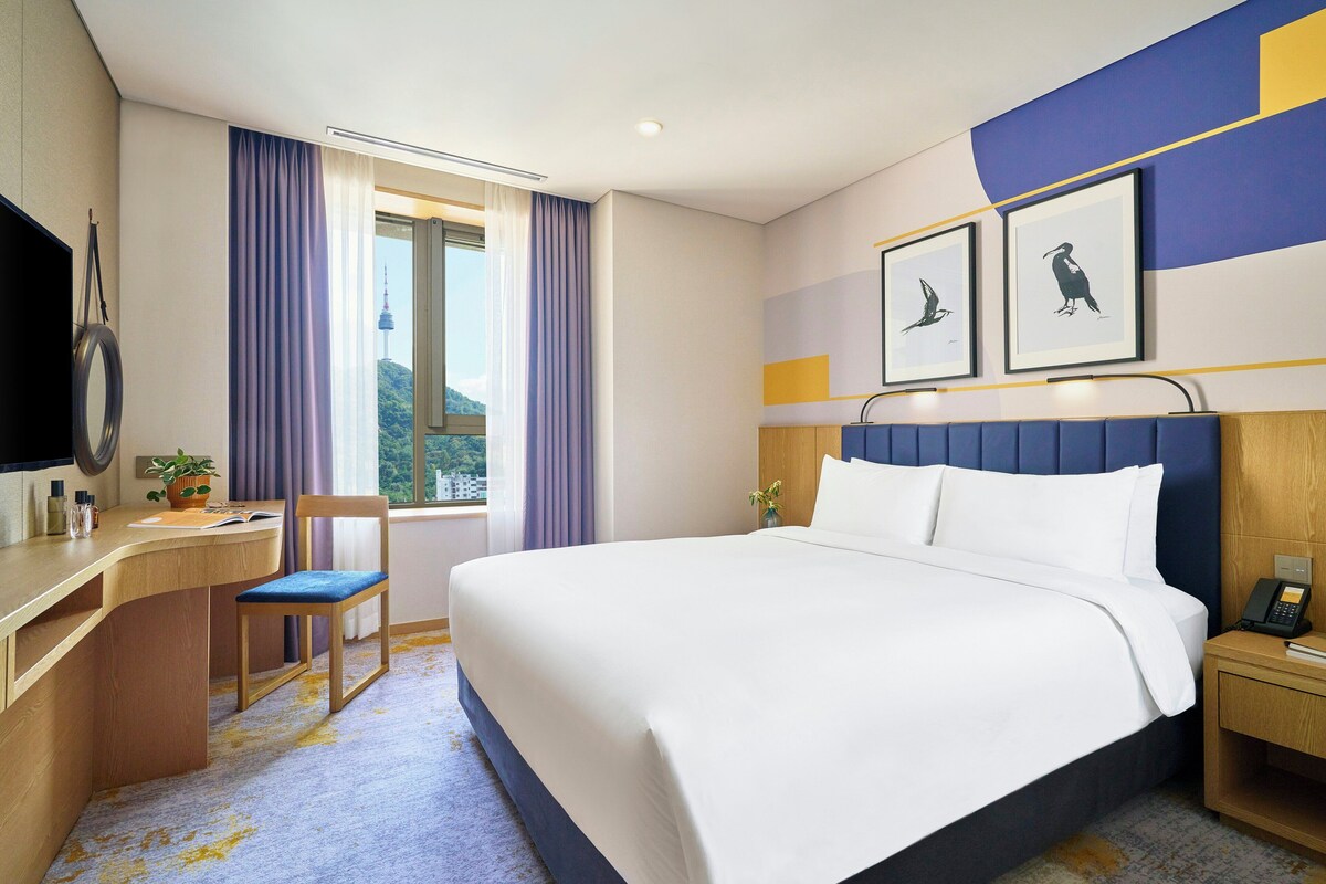 A hotel room with a bed, a desk, a chair, a television, and a window with curtains.