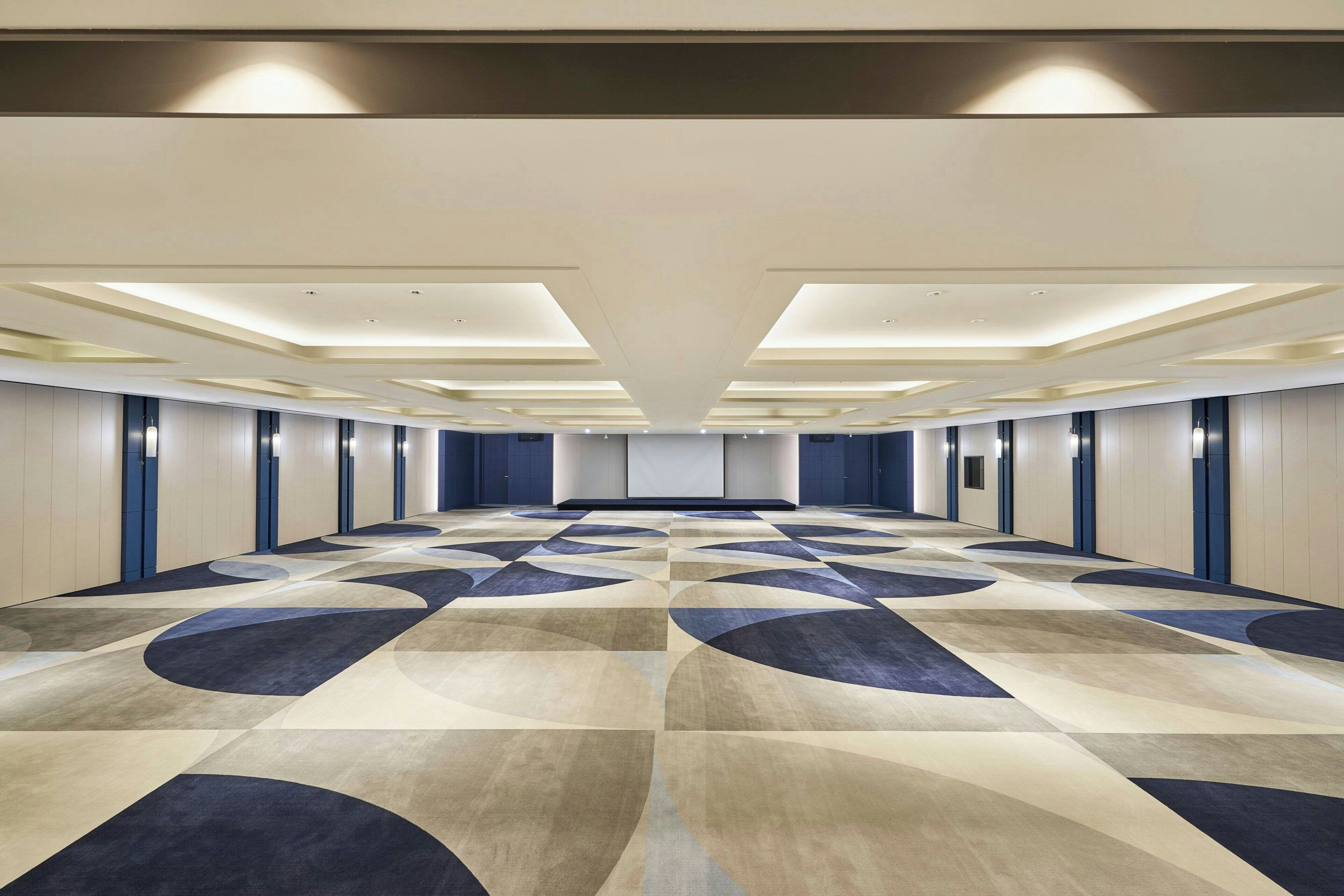 A hotel corridor with a patterned carpet, recessed lighting, and a symmetrical design.