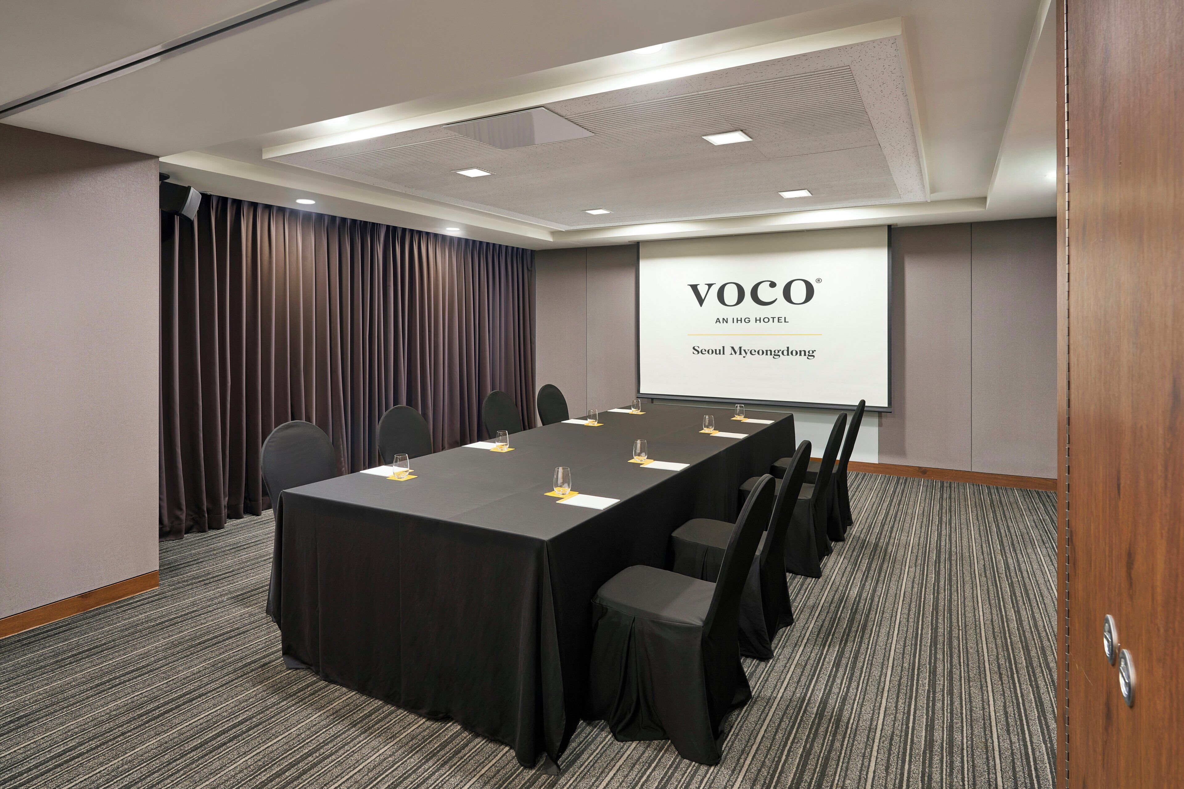 A conference room with a long table, chairs, a projector screen, and a draped curtain.