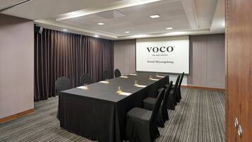 A conference room with a long table, chairs, a projector screen, and a draped curtain.