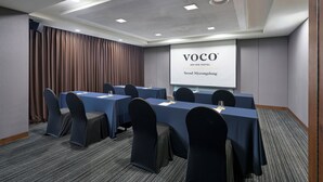 A conference room with a large screen displaying 'VOCO AN IHG HOTEL Seoul Myeongdong'. Tables are set with chairs, and the room has a carpeted floor. - voco Seoul Myeongdong by IHG (Seoul)