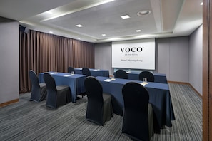 A conference room with a large screen displaying 'VOCO AN IHG HOTEL Seoul Myeongdong'. Tables are set with chairs, and the room has a carpeted floor.