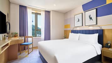 Une chambre d’hôtel avec un lit, un bureau, une chaise, une télévision et une fenêtre avec des rideaux.