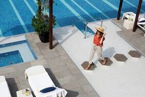Un área junto a la piscina con sillones de descanso, una planta en maceta y una persona caminando.