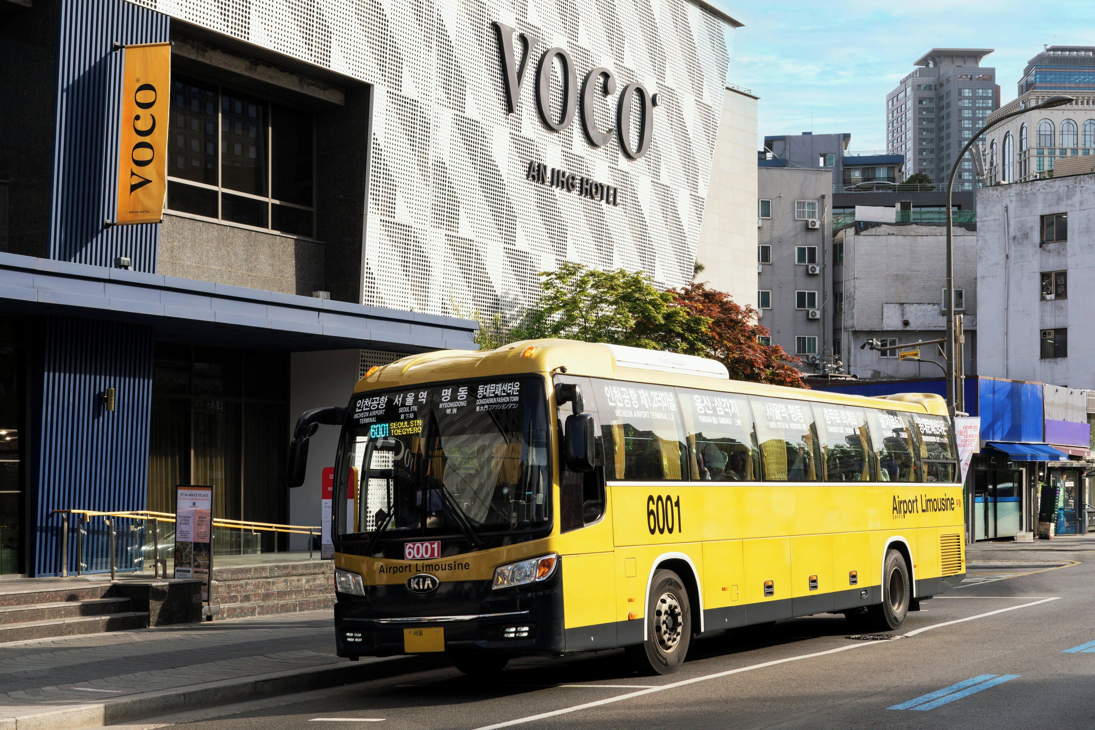 A yellow airport limousine bus with the number 6001 parked in front of a building with a large sign that reads 'YOCO'.