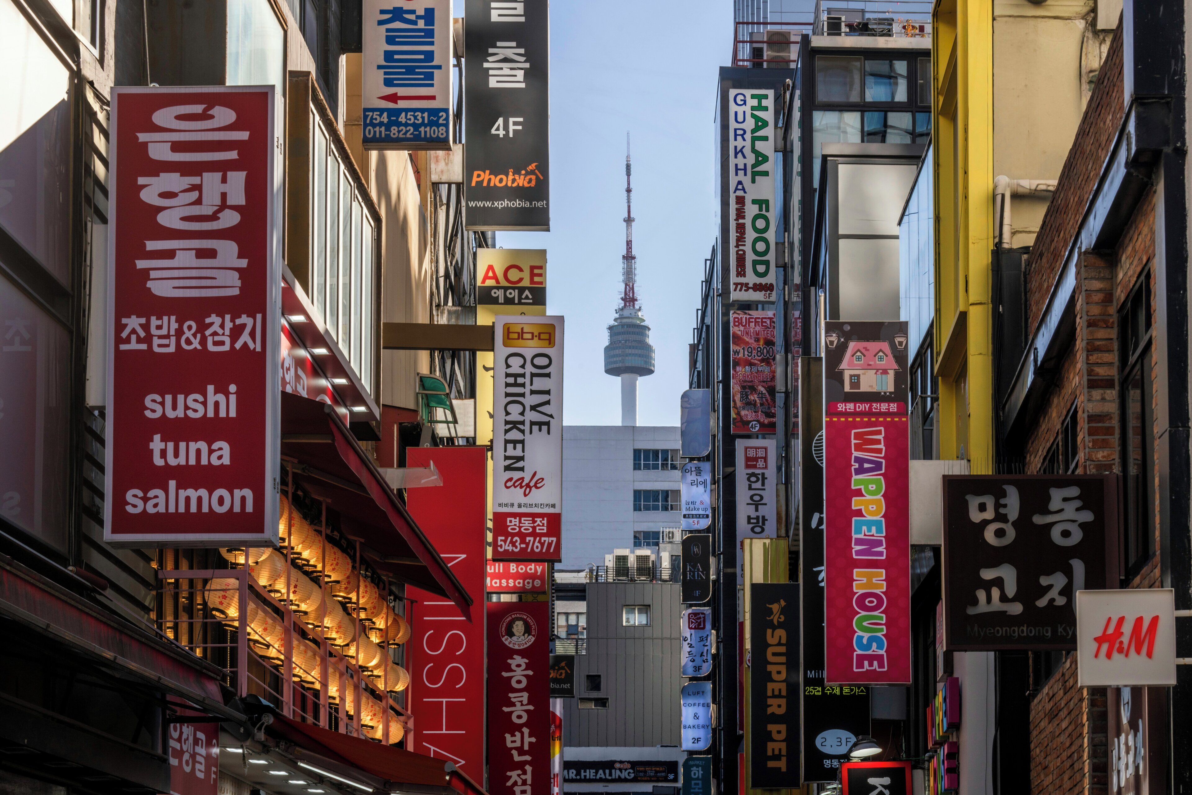 A busy urban street with various commercial signs, including a sushi restaurant and a massage parlor.