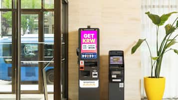 Un espacio interior moderno con un quiosco de pagos, un cajero automático más pequeño y una planta en maceta.
