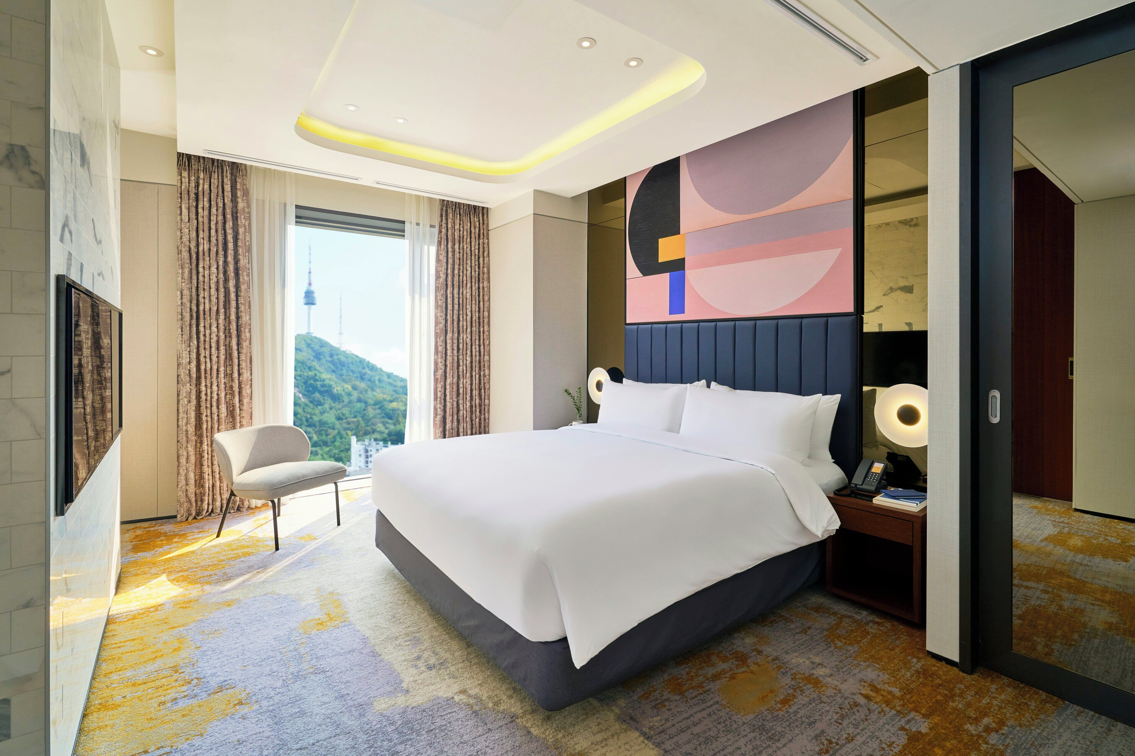A modern hotel room with a large bed, a seating area, and a view of the outdoors.