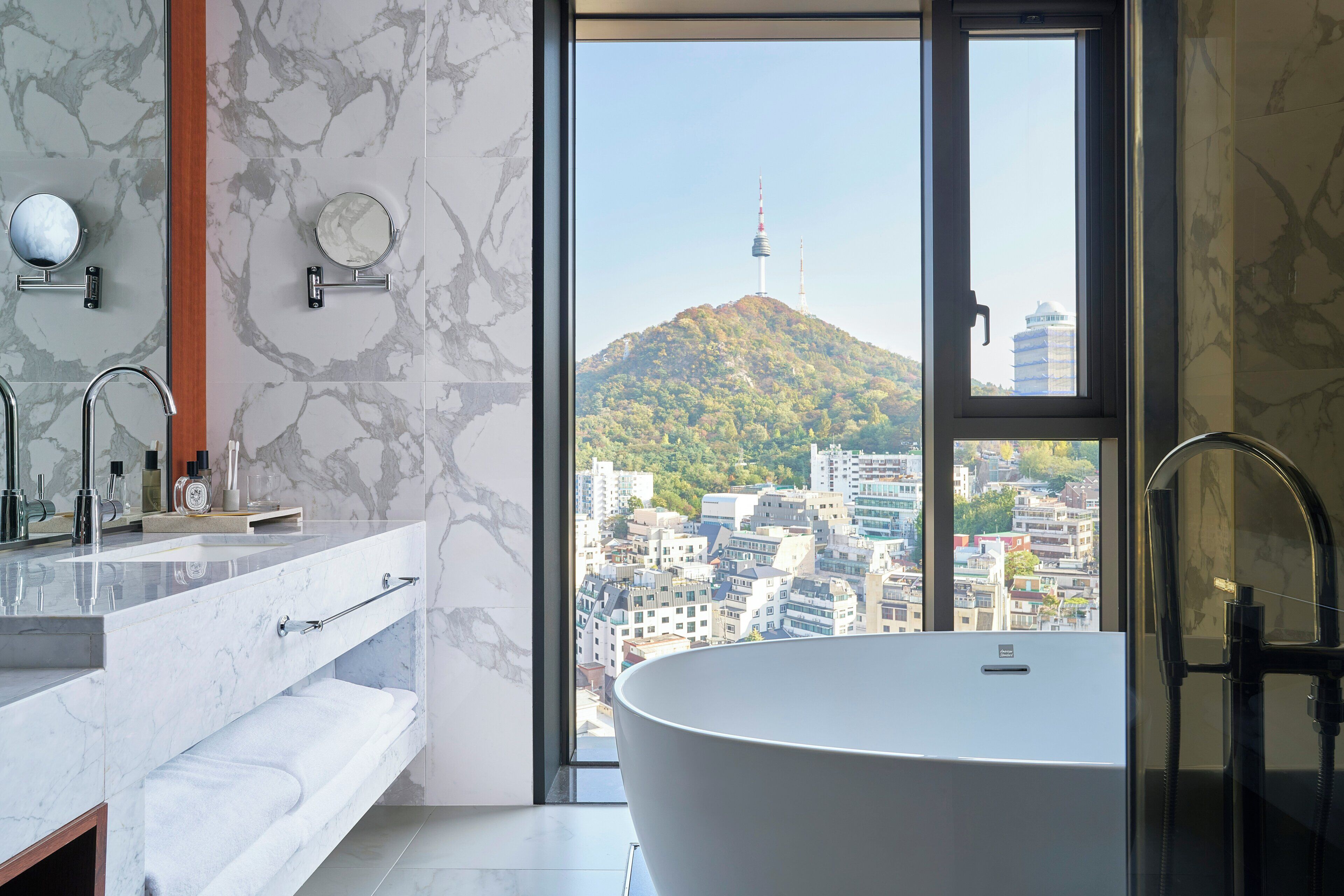 Un baño moderno con una bañera independiente, un tocador con espejo y un amplio ventanal con vistas a la ciudad.