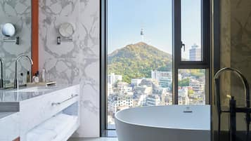 Un baño moderno con una bañera independiente, un tocador con espejo y un amplio ventanal con vistas a la ciudad.