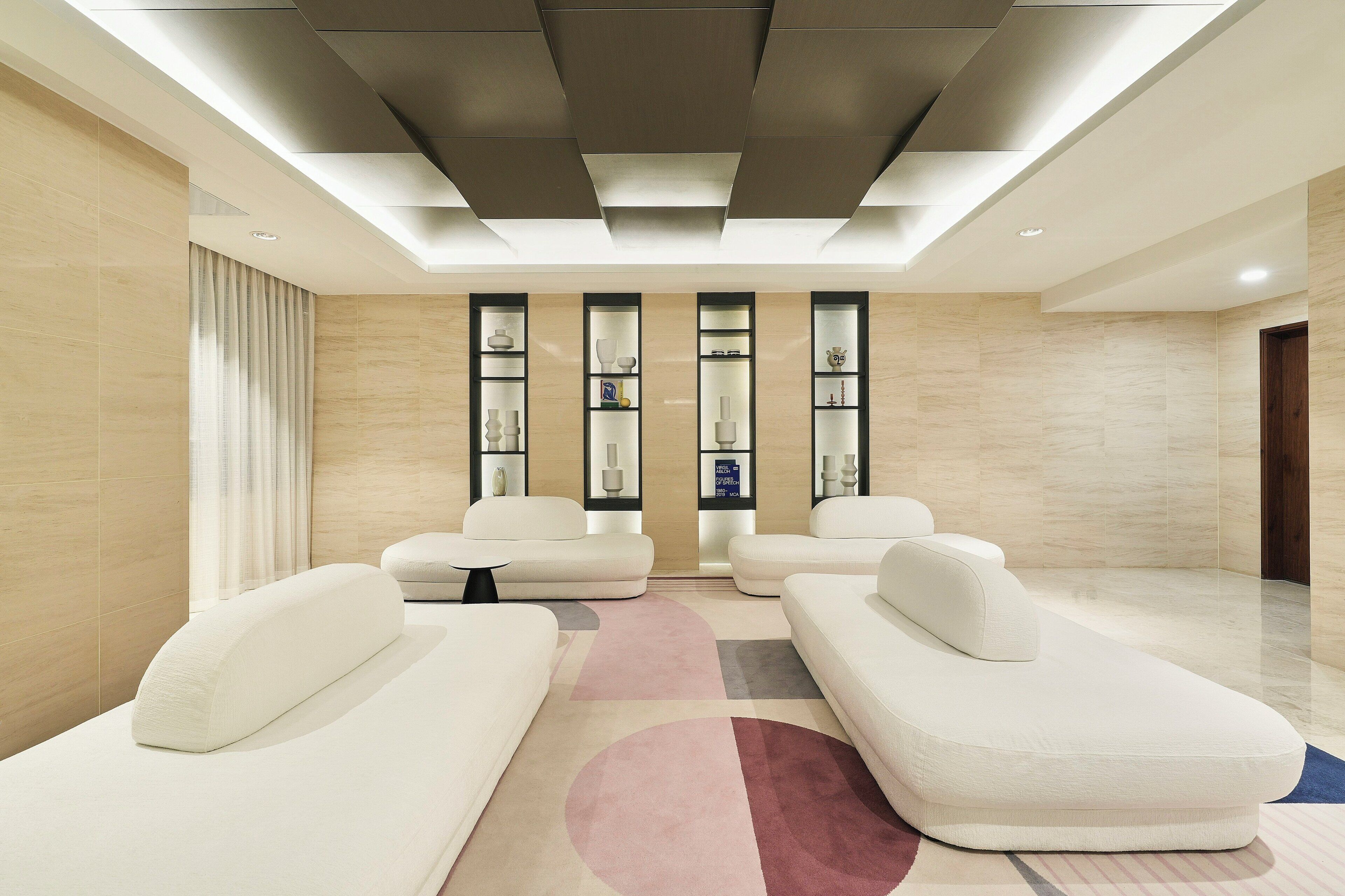 A modern interior with a seating area, a patterned rug, and a wall with vertical shelving displaying decorative items.