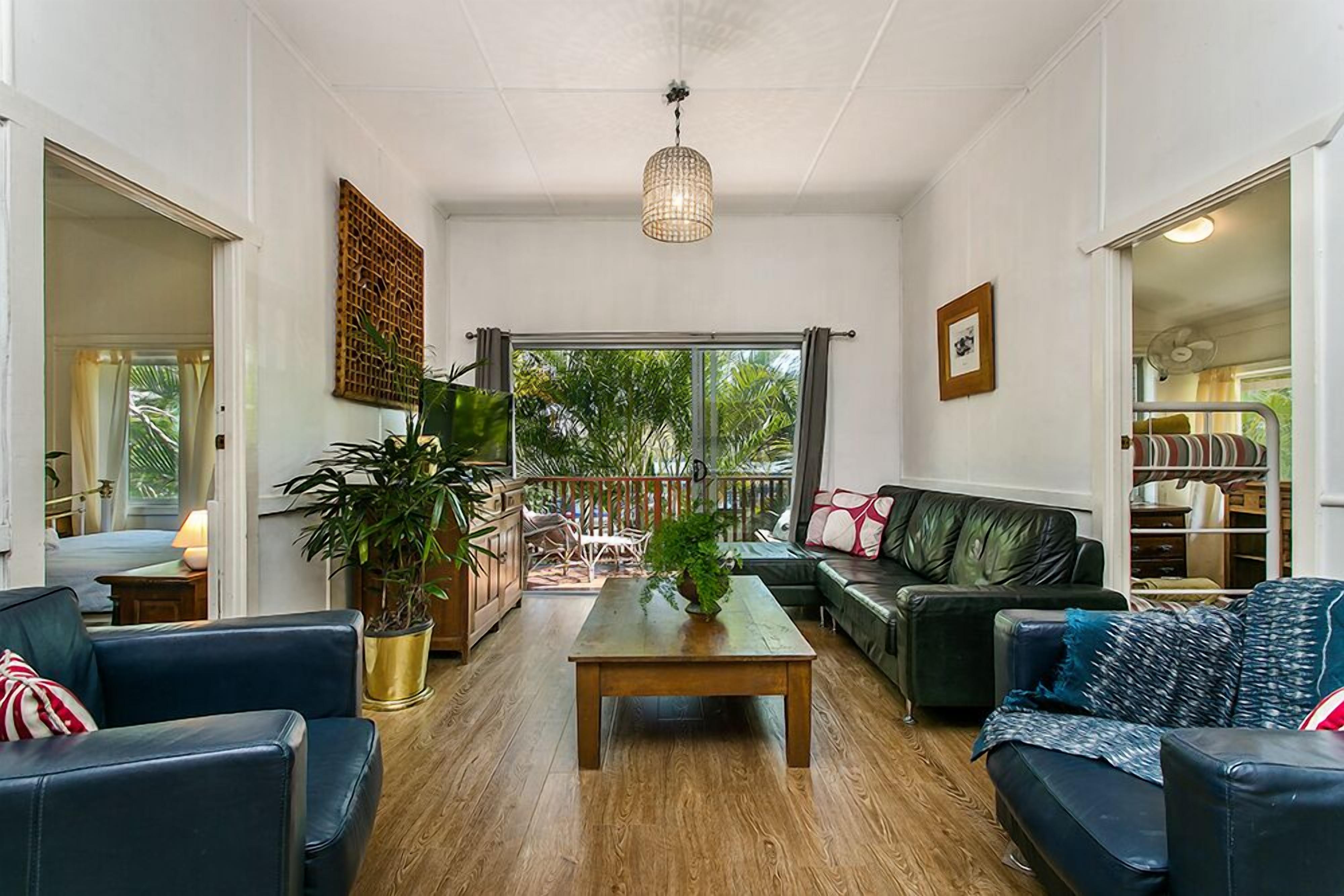A spacious living room with a wooden coffee table, black leather sofas, and a large window offering a view of the outdoors.